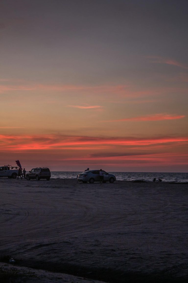 Vehicles parked on a sandy beach during a vivid sunset. Perfect for travel and adventure themes.